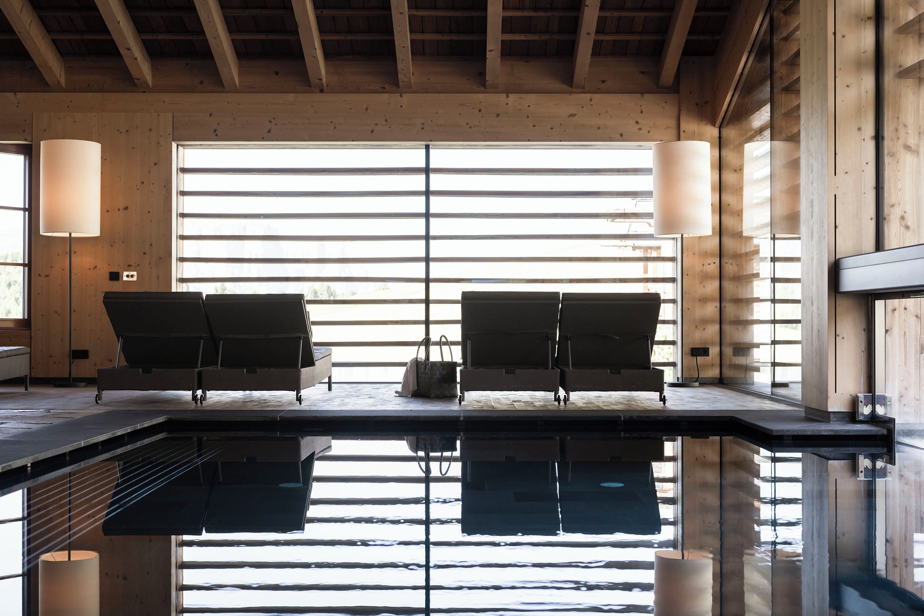 A spa area with two lounge chairs, a large window with blinds, and a reflective pool.