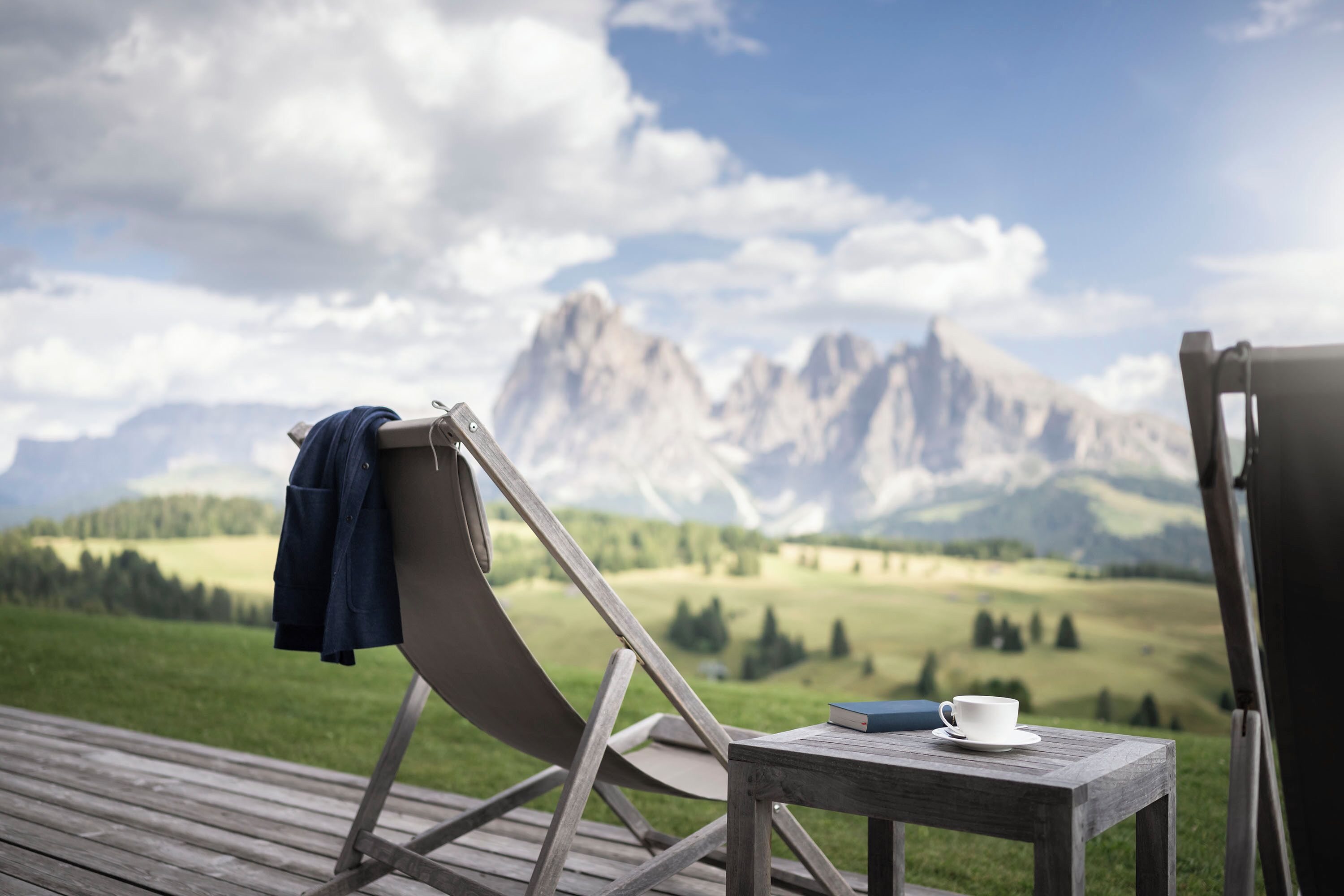 Una terraza de madera con una silla plegable y una pequeña mesa con una taza y un libro.