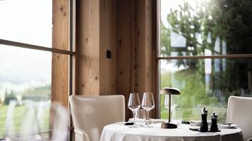 Mesa de comedor con vasos y un molinillo de pimienta, frente a una pared de madera con vistas a follaje.