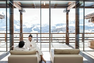 A room with large windows, wooden beams, and a view of snow-covered mountains.