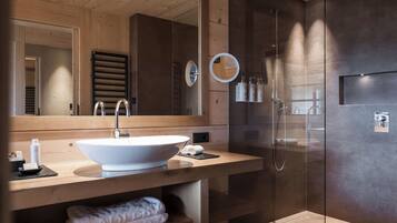 Un baño moderno con techo de madera, un espejo grande, un lavamanos, ducha y zona de ducha con mampara de vidrio.