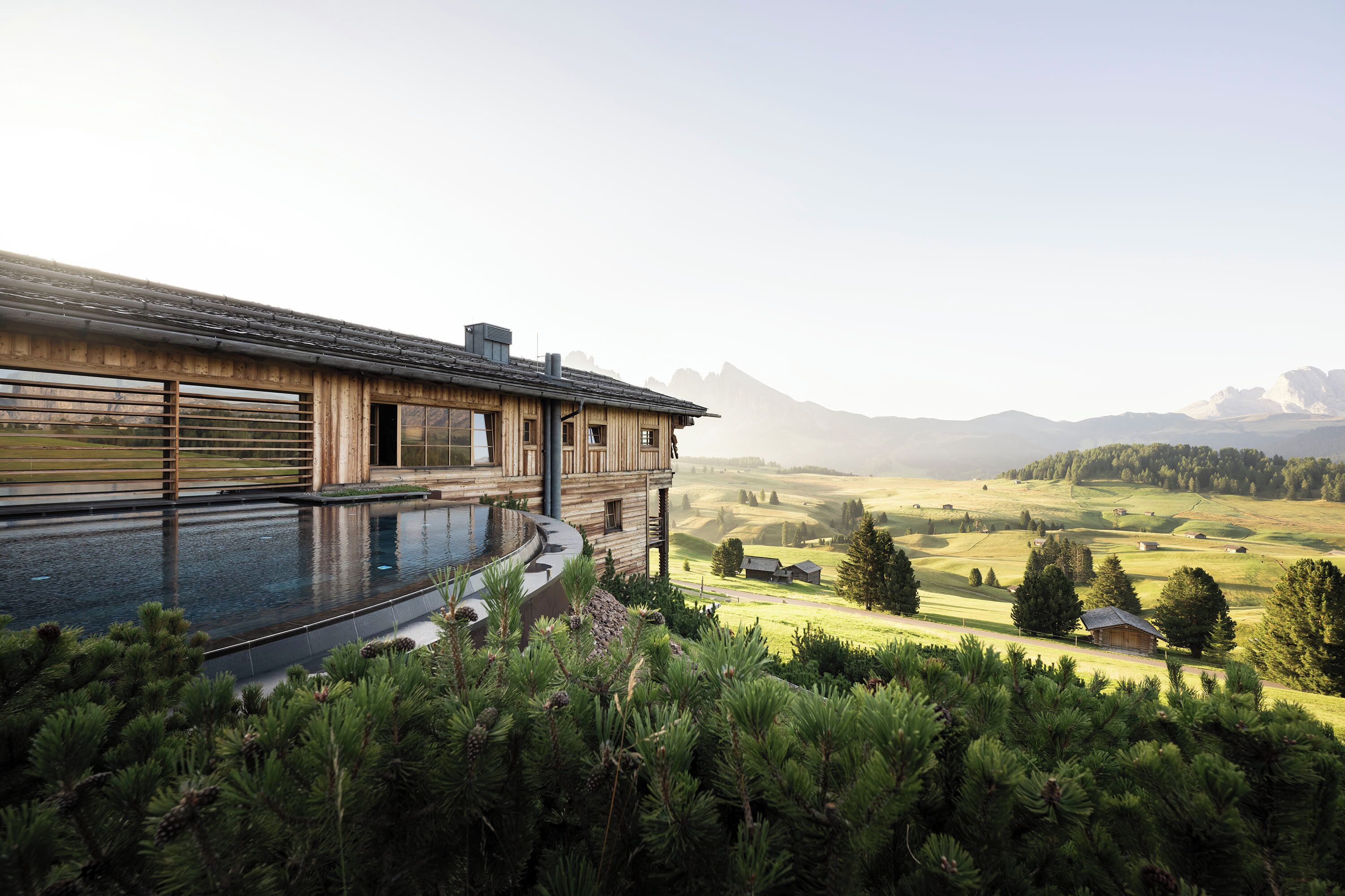 Une grande maison en bois avec une piscine, entourée de pins et offrant une vue sur des collines ondoyantes.