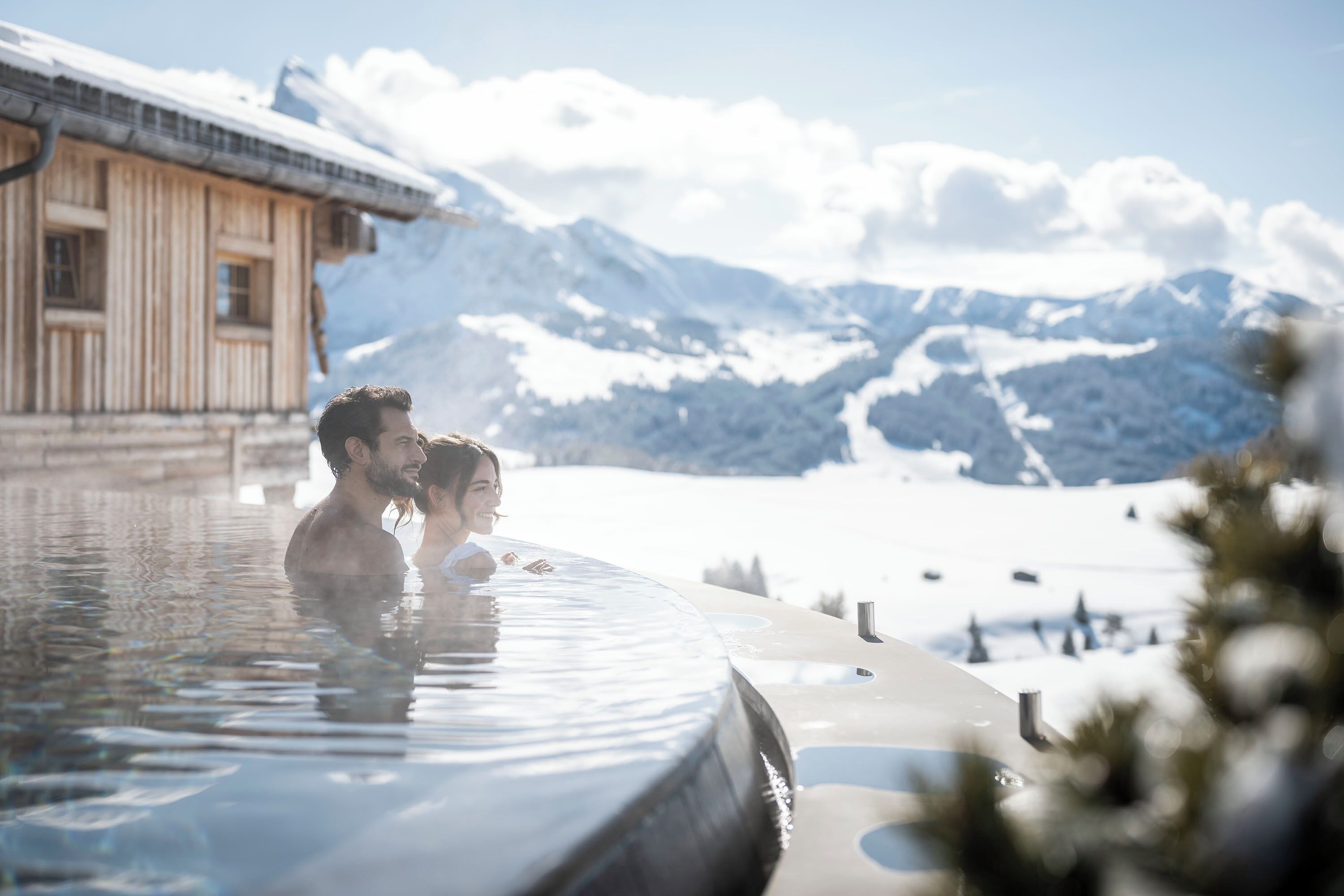 Ein Paar in einer Badewanne vor verschneiten Bergen.
