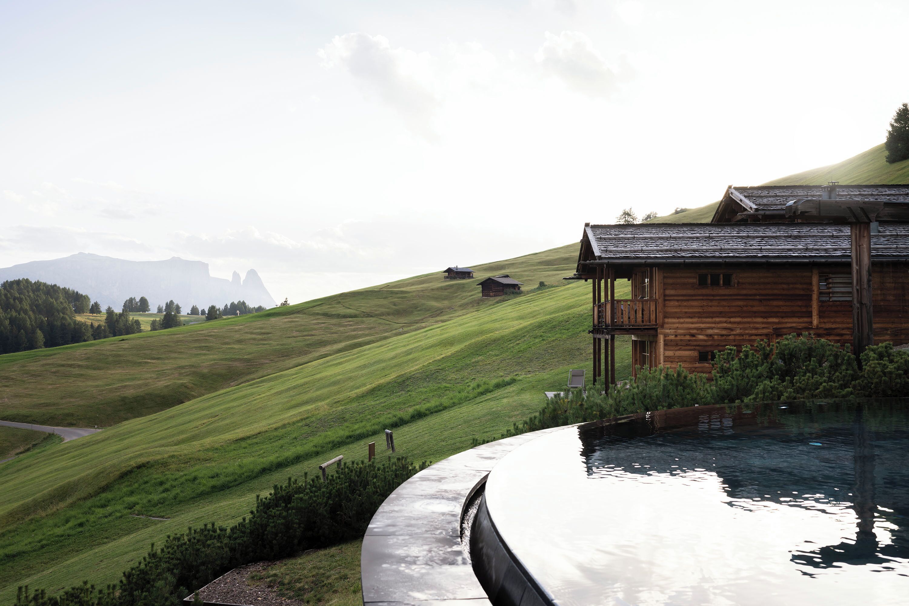 A wooden cabin with a pool, surrounded by a lush green hillside.