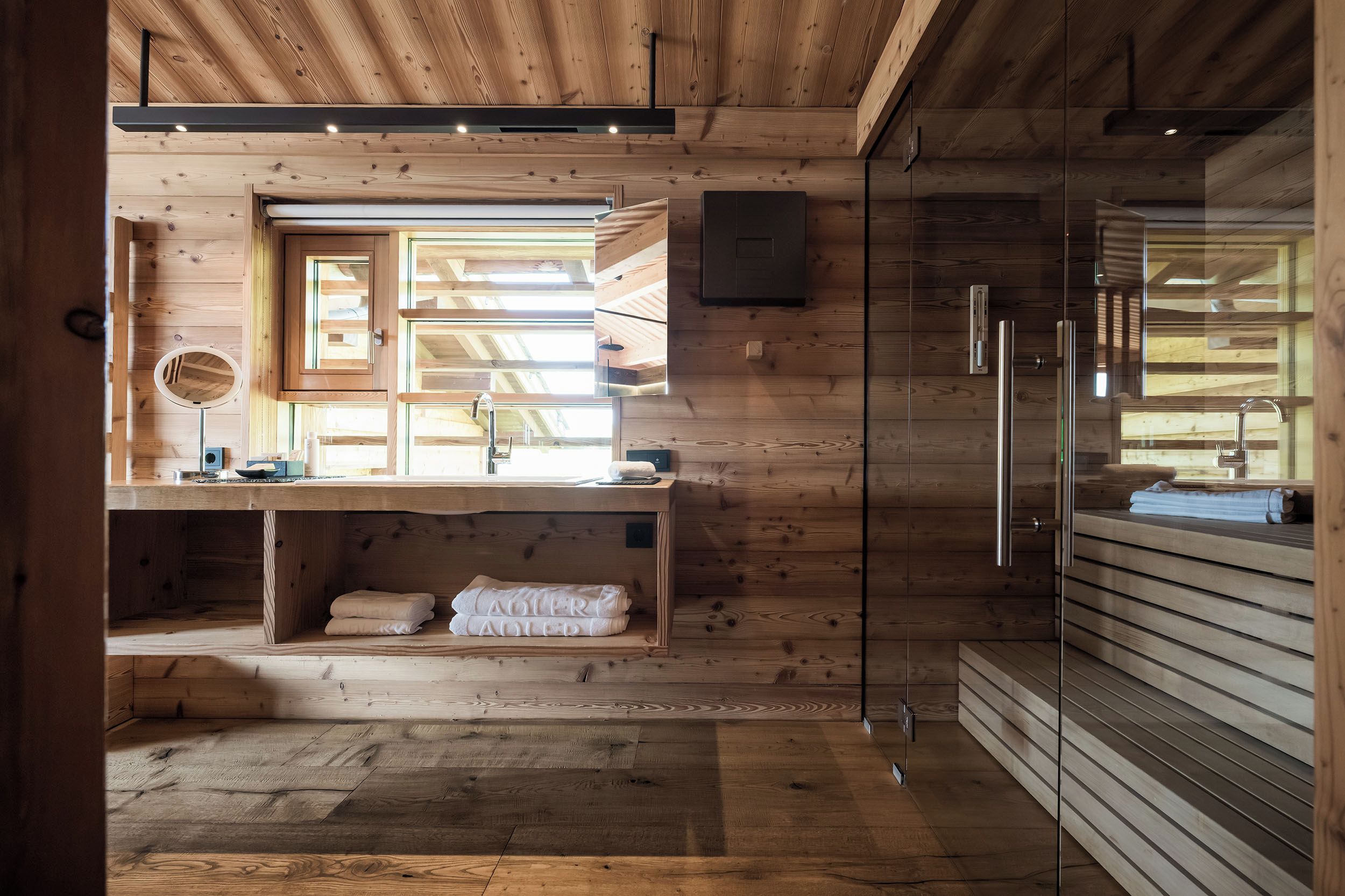 Un interno moderno in legno con lavabo integrato, uno specchio e un porta asciugamani.