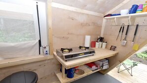 Eine kleine, offene Küche mit einem Gasherd, Holzregalen und einem Fenster.