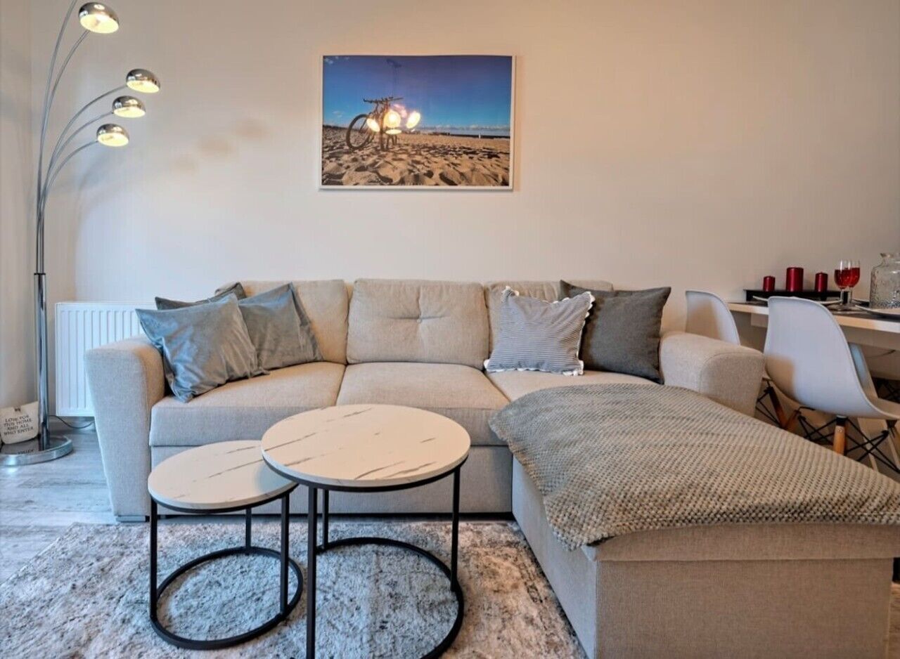 Un salon avec un canapé, deux tables rondes, une lampe et un tableau encadré accroché au mur.