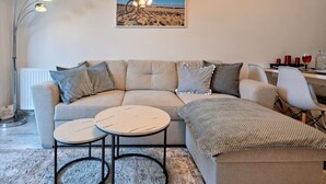 Ein Wohnzimmer mit einer Couch, zwei runden Tischen, einer Lampe und einem gerahmten Bild an der Wand.