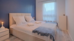 Ein Schlafzimmer mit einem Bett, Nachttischen, einem Fenster mit Vorhängen und einer Deckenleuchte.