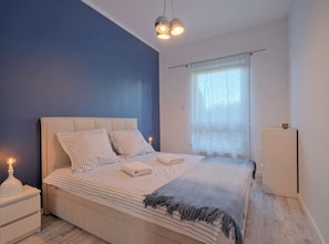 Ein Schlafzimmer mit einem Bett, Nachttischen, einem Fenster mit Vorhängen und einer Deckenleuchte.