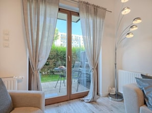 Ein Zimmer mit einer Schiebeglastür, die zu einem Außenbereich führt, einem Sofa, einer Stehlampe und einem Heizkörper.