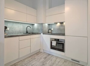 Eine moderne Küche mit weißen Schränken, einem eingebauten Backofen und einer Spüle aus Edelstahl.