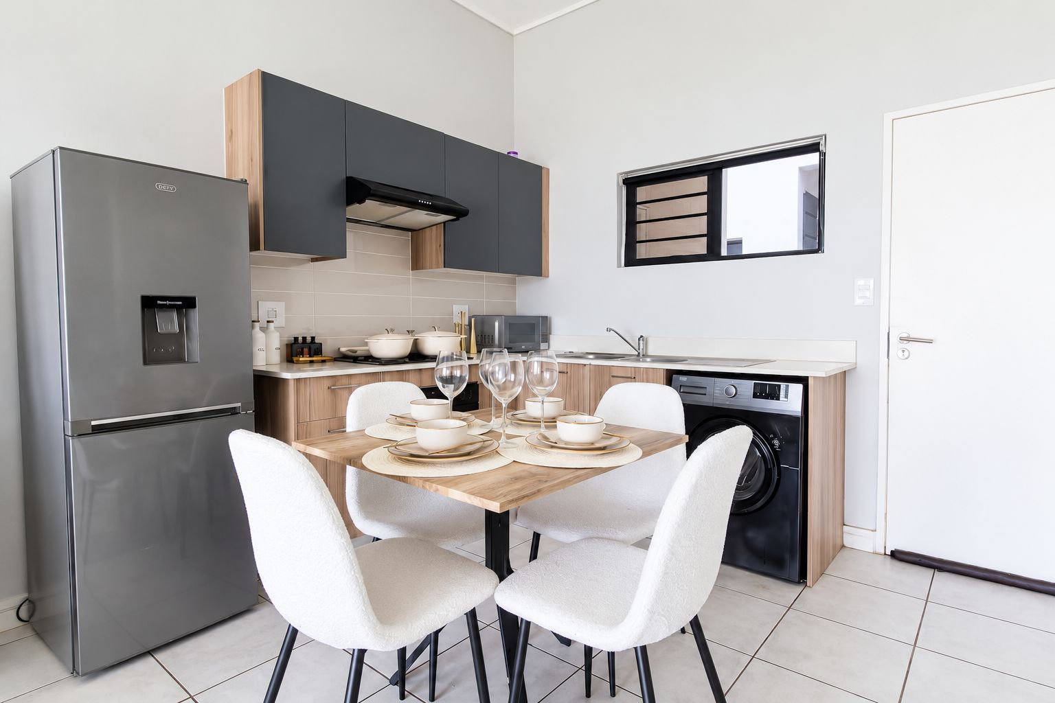Une cuisine compacte équipée d’un réfrigérateur intégré, d’un four à micro-ondes et d’un lave-linge. On y trouve une table à manger avec des chaises, et une fenêtre au-dessus.