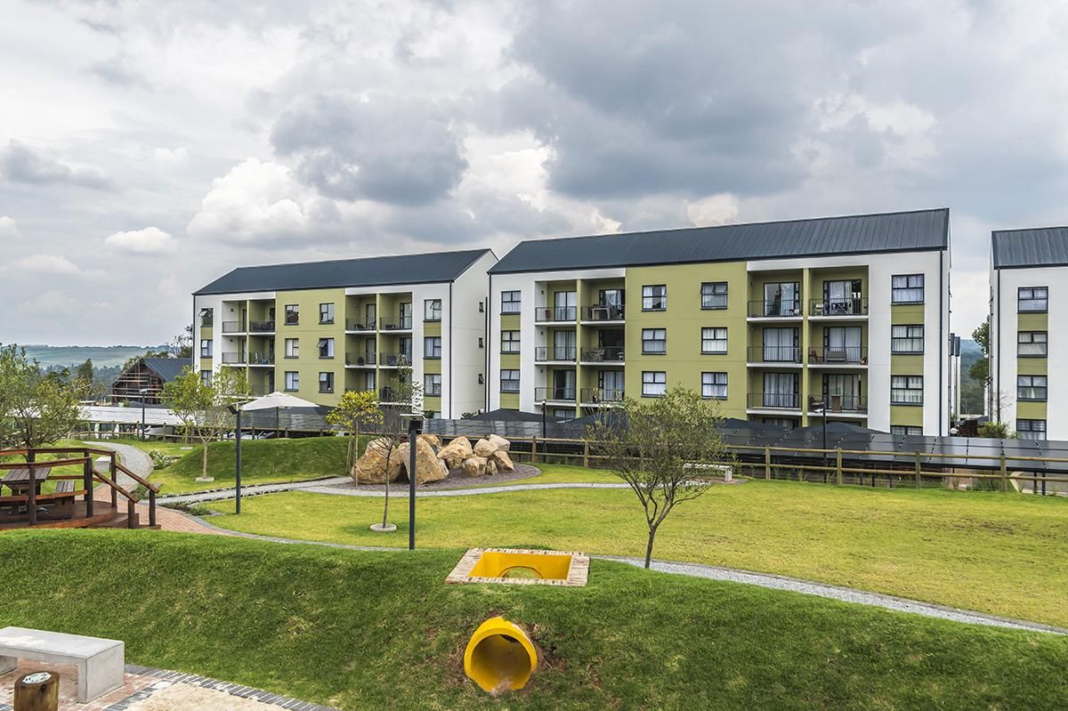 A multi-story residential building with balconies, a grassy area with a playground, and a body of water in the background.