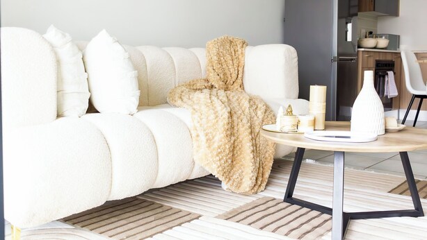 En moderne stue med sofa, rundt sofabord og et køkken i baggrunden.