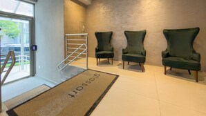 Un vestíbulo moderno con dos sillones verdes, una barandilla de escalera metálica y un felpudo con la palabra 'BOSS'.