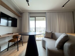 A modern living room with a flat-screen TV, a round table, a sofa, and a balcony with curtains. - GA 127Ape com AR prox. Allianz  (São Paulo)