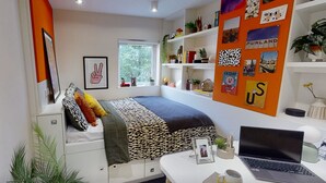 Quarto moderno com cama, escrivaninha com laptop, janela e parede decorada.