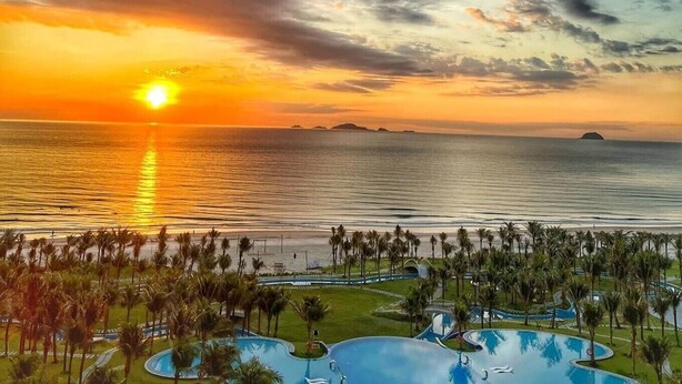 Ein Resort mit Poolanlage, Palmen und Sonnenuntergangsblick über dem Meer.
