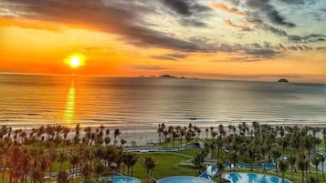 Un complexe hôtelier doté d’une piscine, de palmiers et offrant une vue imprenable sur l’océan au coucher du soleil.