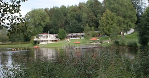 A lakeside hotel with a swimming area, a dock, and a building with a red roof. - Holiday Apartment "Am Hennenberg" Between Allgäu, Ulm, and Lake Constance (Erlenmoos)
