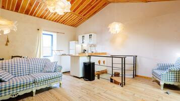A cozy room with a wooden ceiling, a kitchenette, a sofa, and a dining table.