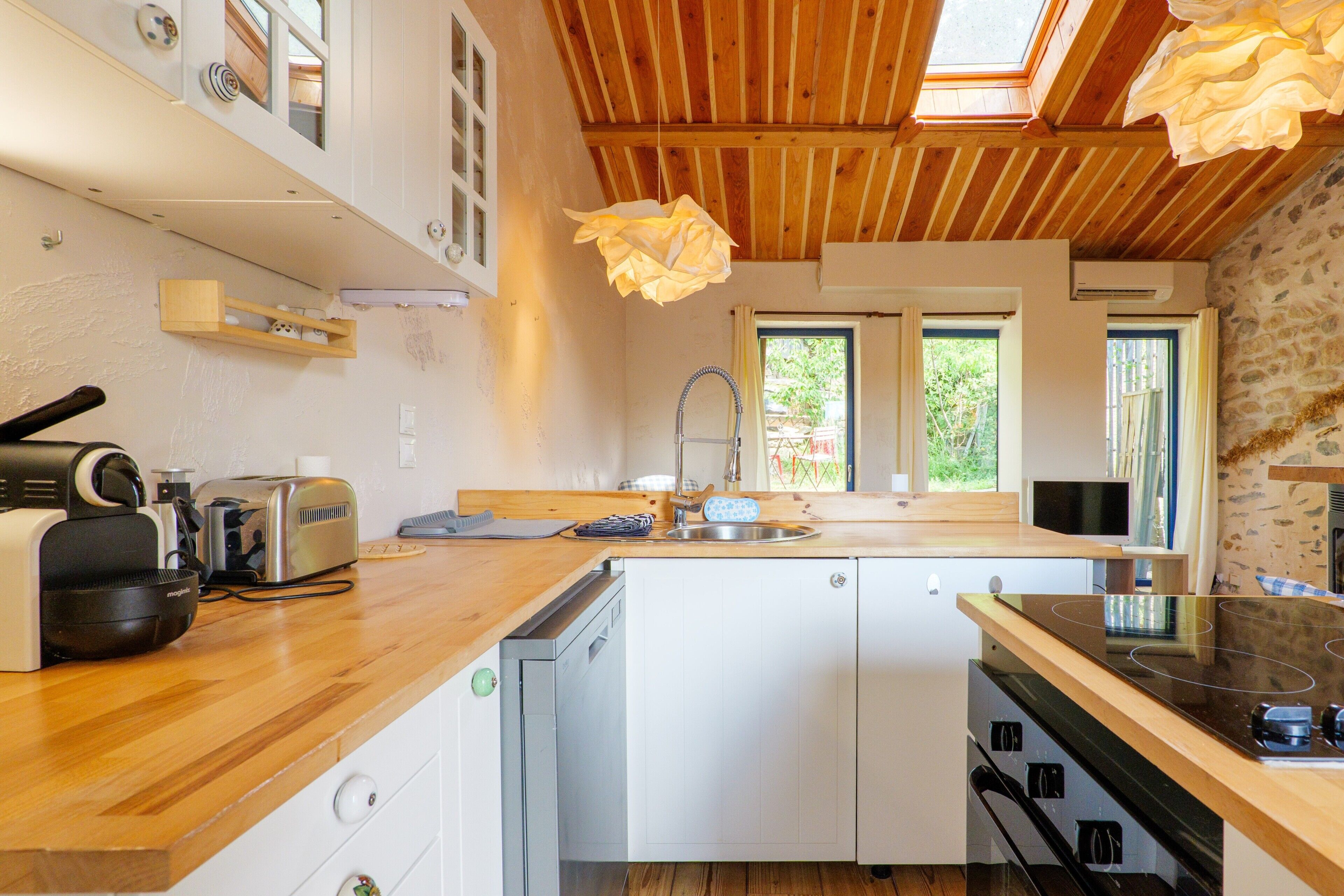 A compact kitchen with a wooden countertop, a dishwasher, a stove, and a window with a view of greenery.