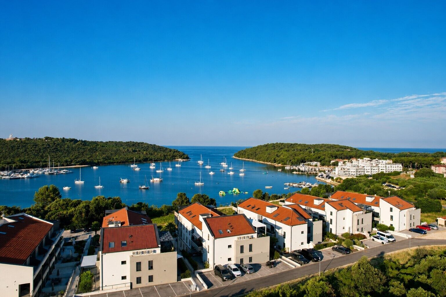 A coastal town with modern buildings, a marina with boats, and a clear blue sky.