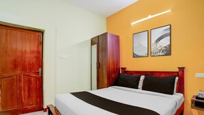 A hotel room with a bed, wooden wardrobe, and two wall-mounted artworks. - Classic Zamindar Heritage (Puducherry)