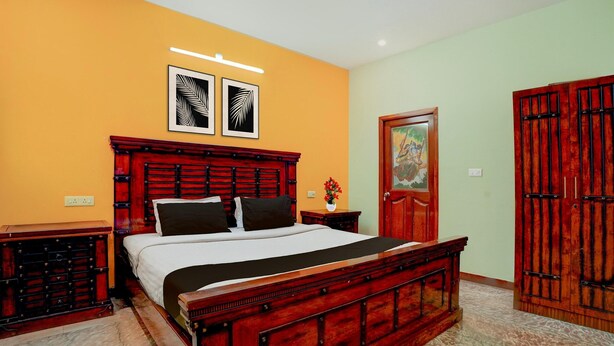 A bedroom with a wooden bed, a nightstand, a wall-mounted light, and a door with a decorative panel. - Classic Zamindar Heritage (Puducherry)