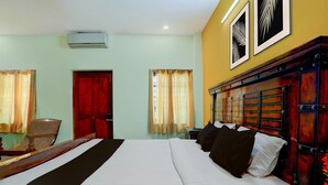 A hotel room with a large bed, a wooden headboard, a red door, and two windows with curtains. - Classic Zamindar Heritage (Puducherry)