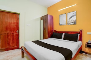 A hotel room with a bed, wooden wardrobe, and two wall-mounted artworks. - Classic Zamindar Heritage (Puducherry)