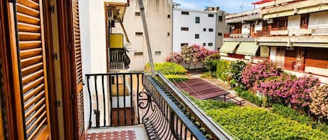 A balcony with a red patterned floor, a metal railing, and a view of neighboring buildings and greenery.