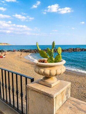 Ein Strand mit einem Kakteenbeet im Vordergrund, einem Felsstollen und Personen im Hintergrund.