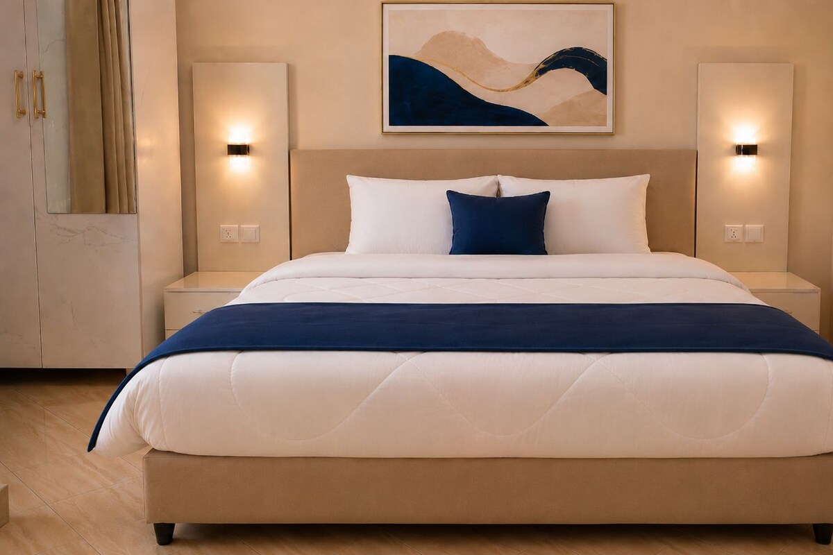 A hotel room with a large bed, two bedside lamps, a nightstand, and a wall-mounted artwork.