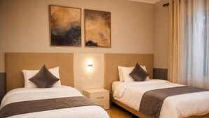 Two beds with headboards, a nightstand, a wall-mounted light, and two abstract paintings.
