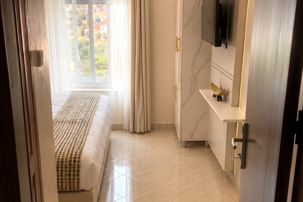 A modern bedroom with a bed, a TV mounted on the wall, and a bathroom with a shower.