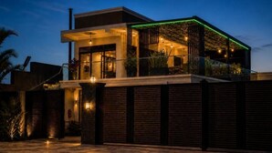 A modern two-story building with a flat roof, large windows, and a balcony with green lighting.