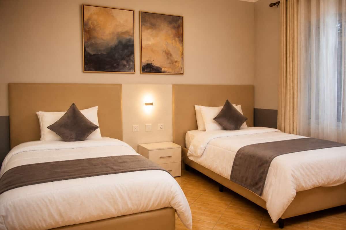 Une chambre d’hôtel avec deux lits, une table de chevet, une lampe fixée au mur et une fenêtre avec des rideaux.