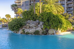 A pool surrounded by lush greenery and a rocky island. - 3BR Edgewater Condo | Pools, Golf, Tennis & Private Beach Access! (Panama City Beach)