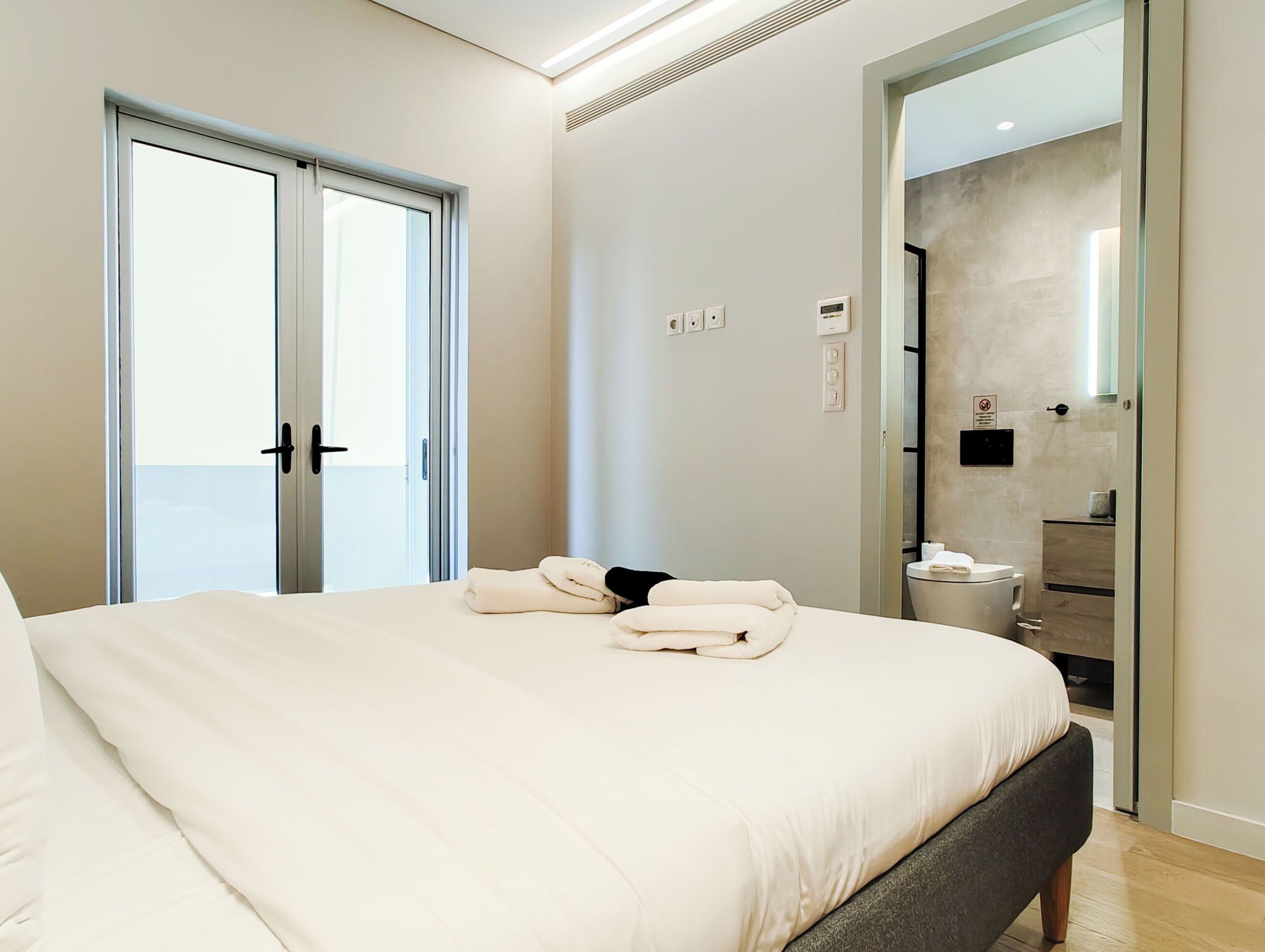 Une chambre avec un lit, une salle de bain avec des toilettes et un lavabo, et une porte-fenêtre coulissante.