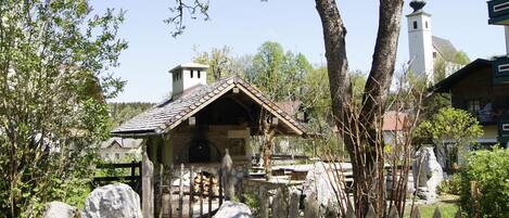 A rustic stone building with a tiled roof, surrounded by trees and a stone fence.