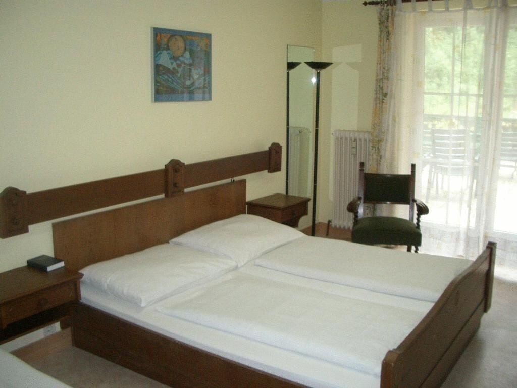 A bedroom with a wooden bed, a nightstand, a chair, a mirror, and a painting on the wall.