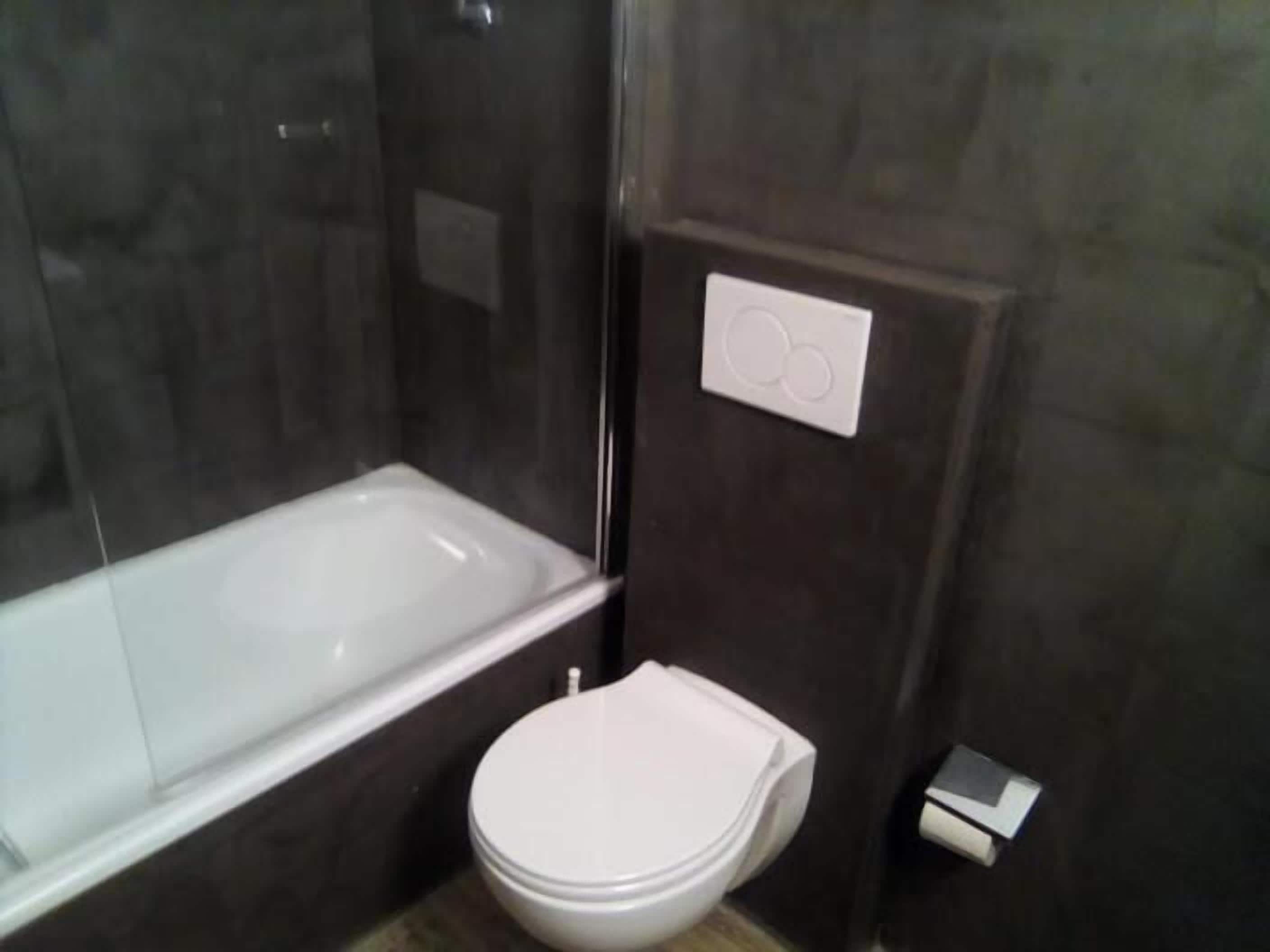 Ein Badezimmer mit Badewanne, Toilette und Bedienfeld an der Wand.