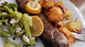 Une assiette contenant du poisson rôti, des brocolis et des tranches de citron.