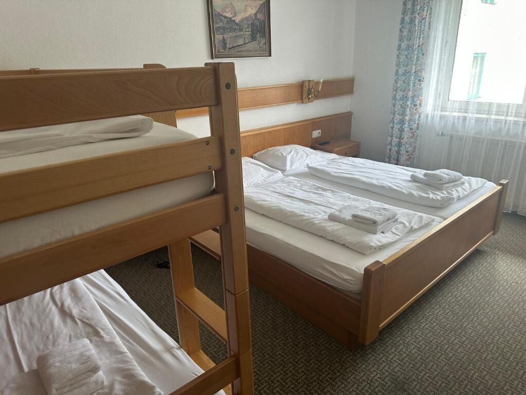Habitación de hotel con literas, cama individual, mesita de noche y ventana con cortinas.
