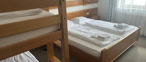 Habitación de hotel con literas, cama individual, mesita de noche y ventana con cortinas.