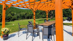 An outdoor seating area with a pergola structure, a table, and chairs.