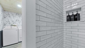 A bathroom with white brick walls, a white sink, and a shelf with three bottles.