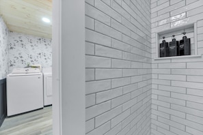A bathroom with white brick walls, a white sink, and a shelf with three bottles.